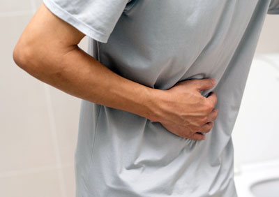 Man holding lower abdomen in discomfort, possibly related to digestive issues like gastroparesis or gastric emptying problems.