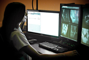 Doctor reviewing radiology images on multiple computer screens.